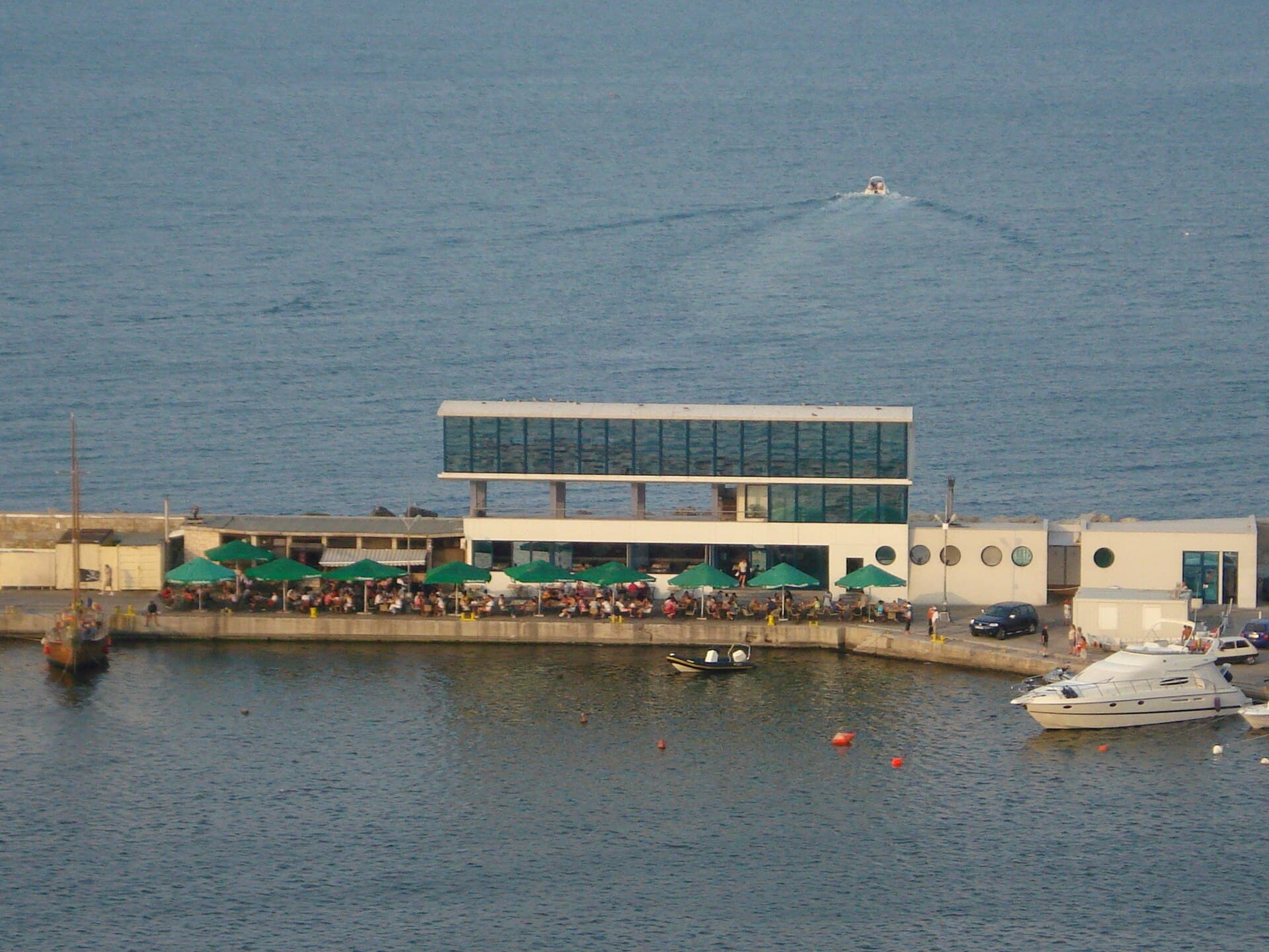 Se vede un terminal de pasageri pe malul mării, cu ambarcațiuni în port. (Foto: Razvan85 / CC BY-SA 3.0, Wikimedia Commons)