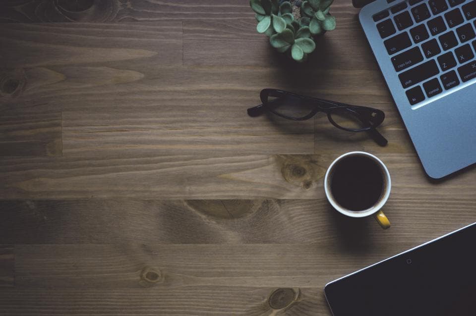 Un birou cu laptop, o tabletă, ochelari, o ceașcă de cafea și o plantă. (Foto ilustrativă: Lia Leslie / CC0 1.0, Openverse)
