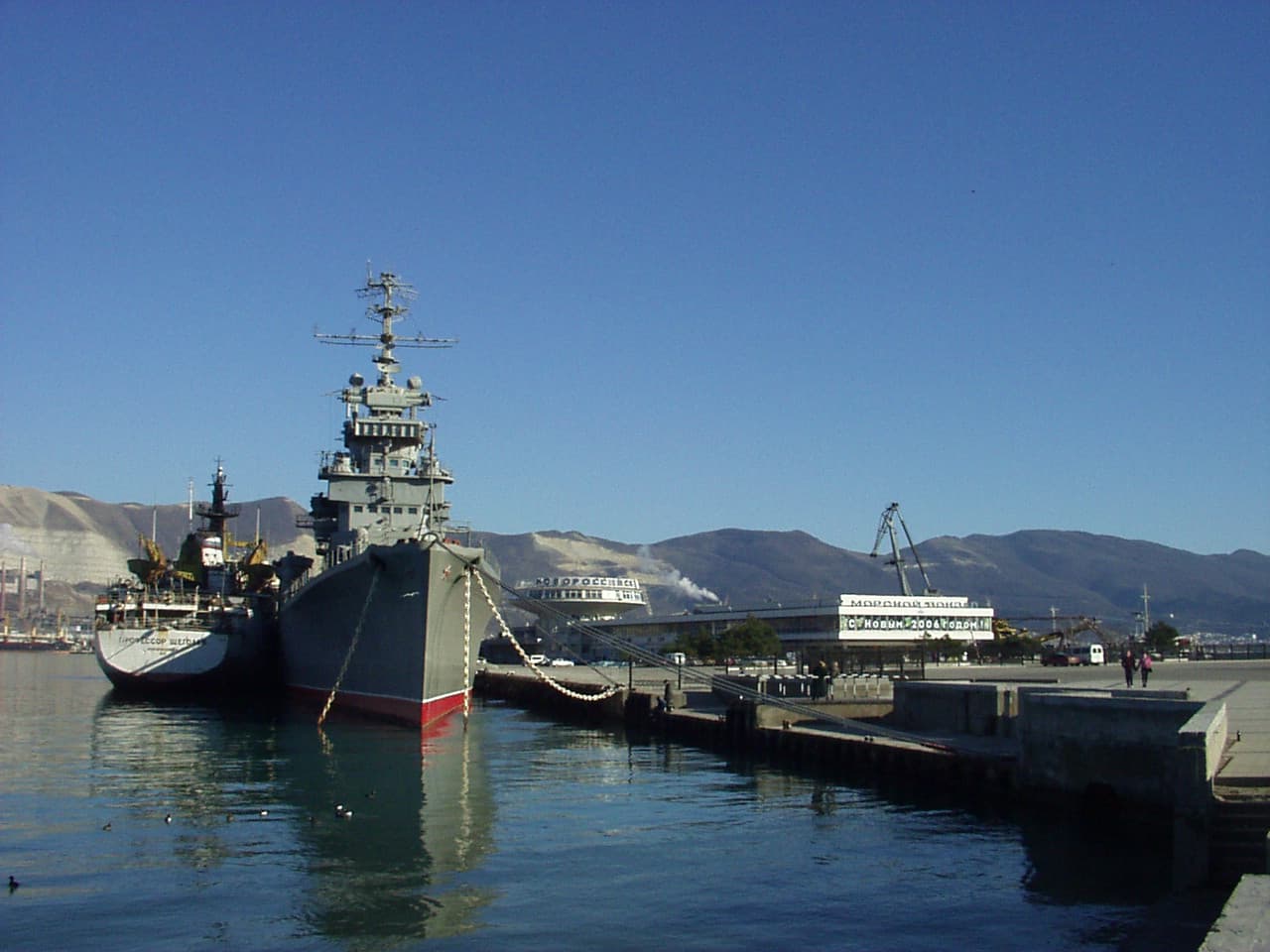 Un port maritim cu nave militare acostate la cheu, într-un peisaj montan. (Foto: ssr ( talk ) / Public domain, Wikimedia Commons)