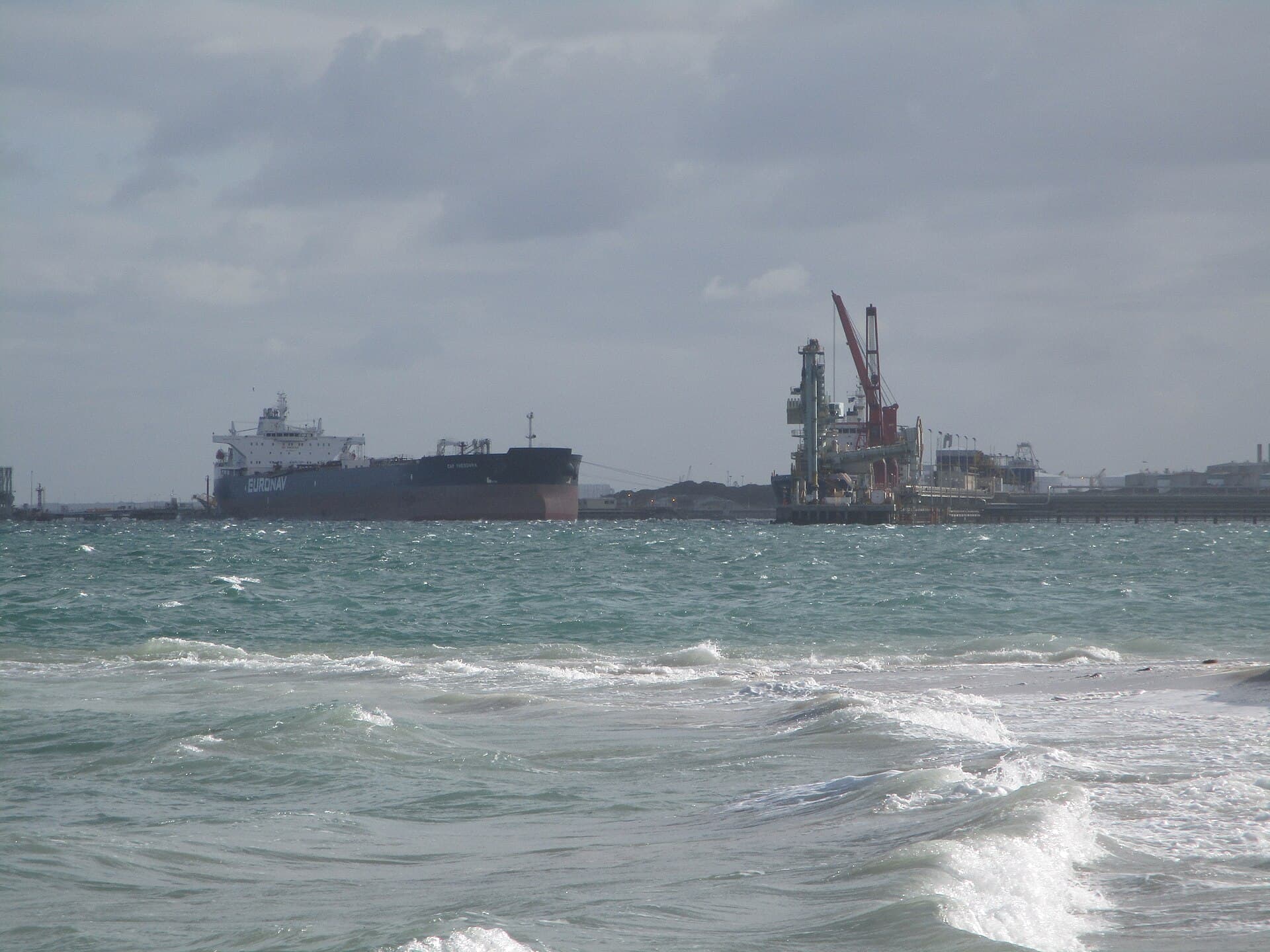 Un petrolier și instalații industriale portuare, văzute de pe țărm, pe mare. (Foto de arhivă: Calistemon / CC BY-SA 4.0, Wikimedia Commons)