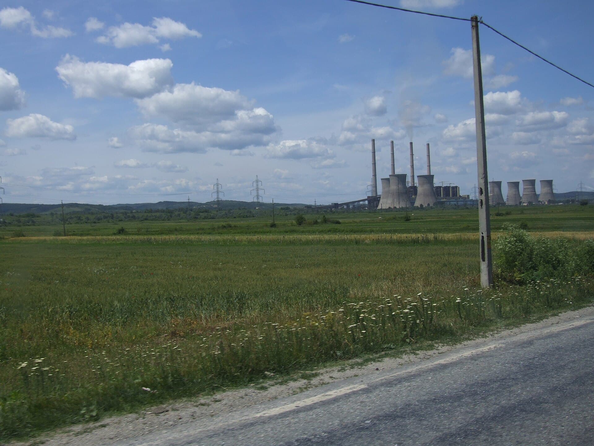 O centrală electrică cu coșuri de fum și turnuri de răcire, văzută dintr-o zonă rurală. (Foto: CristianChirita / CC BY-SA 2.5, Wikimedia Commons)