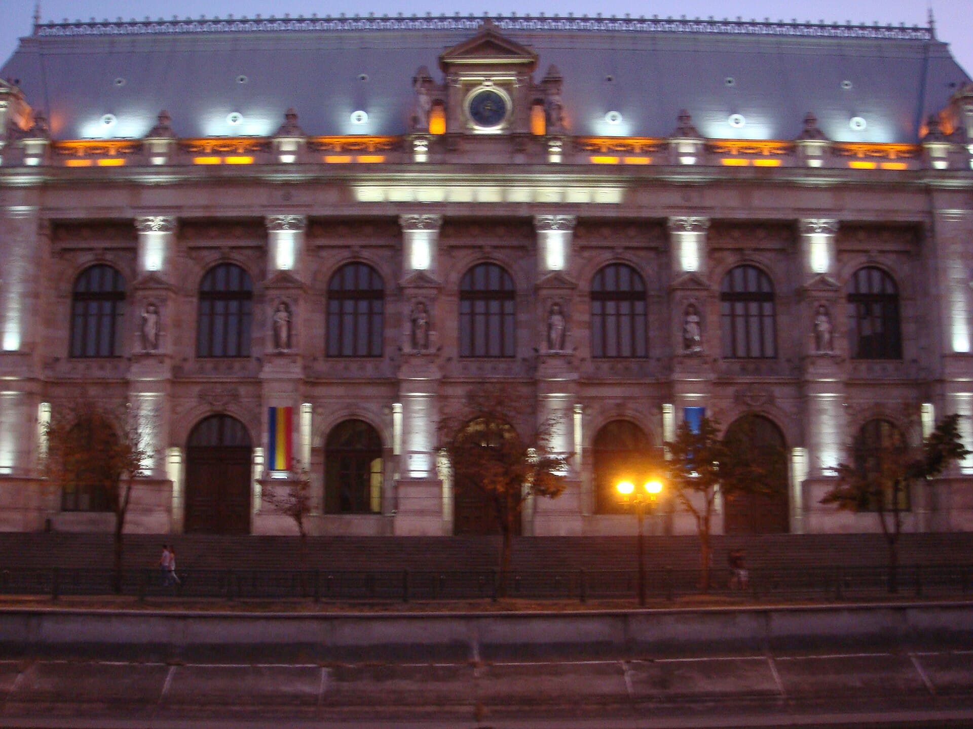 Clădire monumentală a unei instanțe de judecată din București, iluminată seara, cu steagul României la intrare. (Foto: Korinna / CC BY-SA 3.0 ro, Wikimedia Commons)