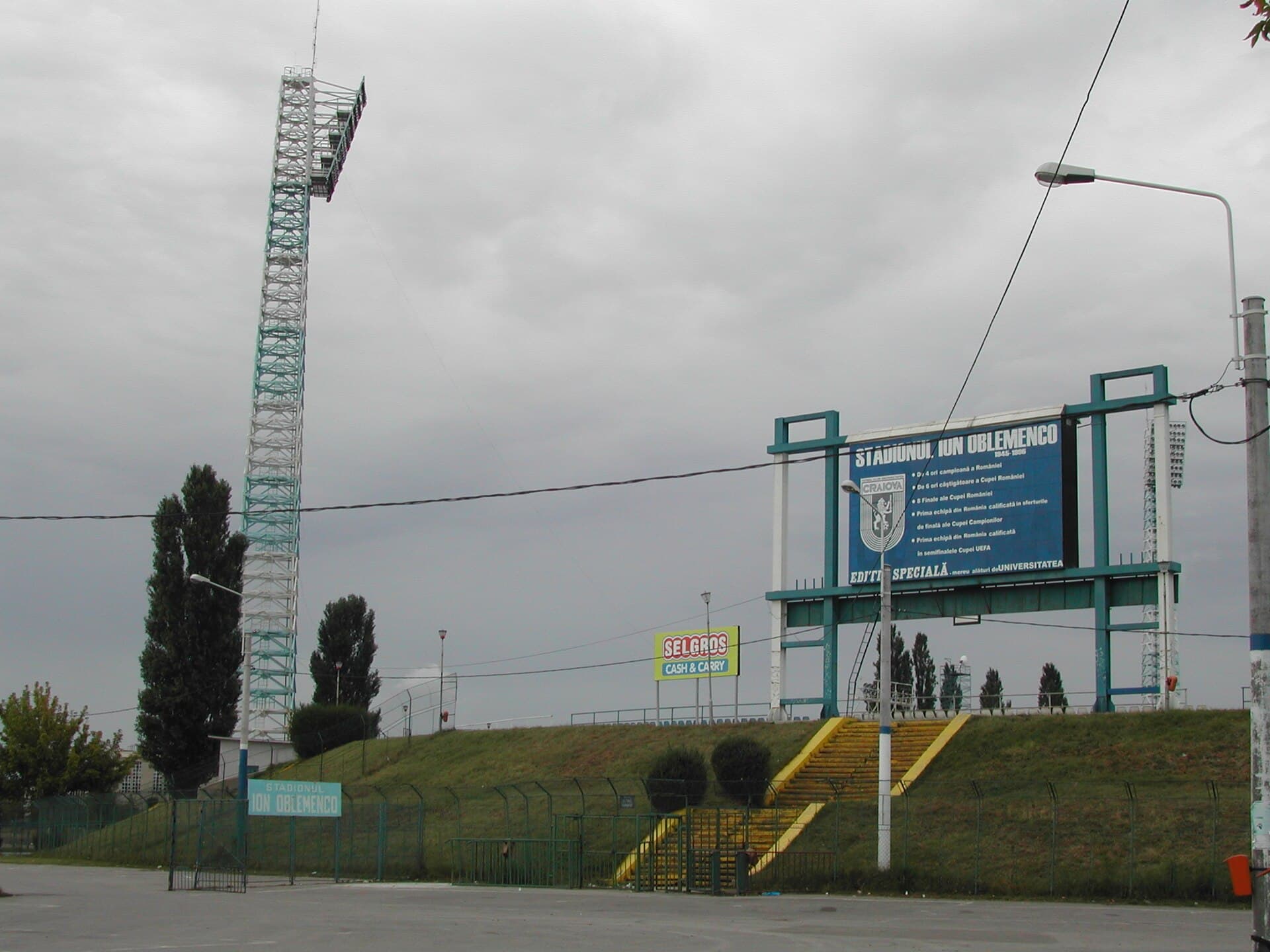 Se vede stadionul și intrarea în baza sportivă a Universității Craiova, cu tabela și instalația de nocturnă. (Foto: Christopher Voitus / CC BY-SA 3.0, Wikimedia Commons)