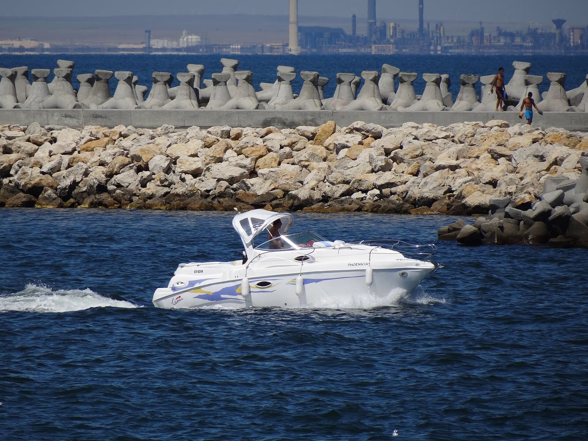 O ambarcațiune pe Marea Neagră, lângă un dig și o zonă industrială de coastă. (Foto: Photopro Pro / CC BY-SA 3.0, Wikimedia Commons)