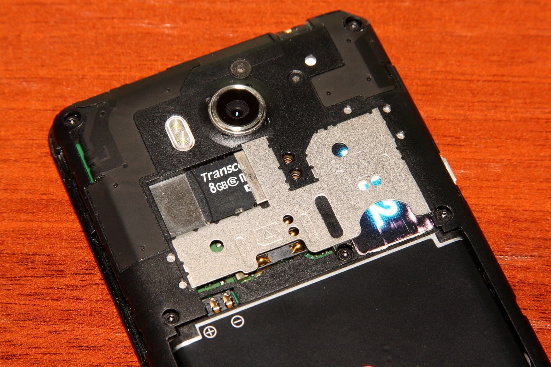 Un telefon mobil desfăcut, cu bateria, camera și componentele interne vizibile, așezat pe o suprafață din lemn. (Foto de arhivă: Ilya Plekhanov / CC BY-SA 3.0, Wikimedia Commons)