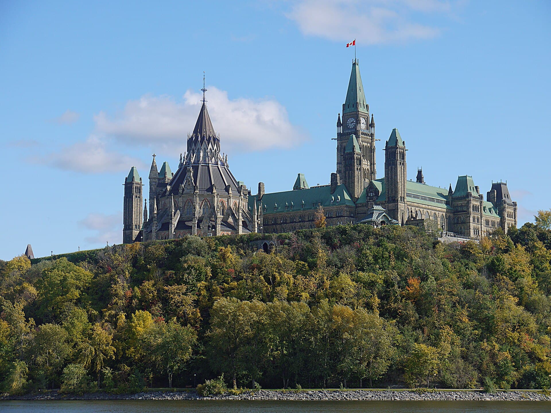 Se vede Parlamentul Canadei din Ottawa, cu steagul canadian, fotografiat de pe malul apei. (Foto: Óðinn / CC BY-SA 2.5 ca, Wikimedia Commons)