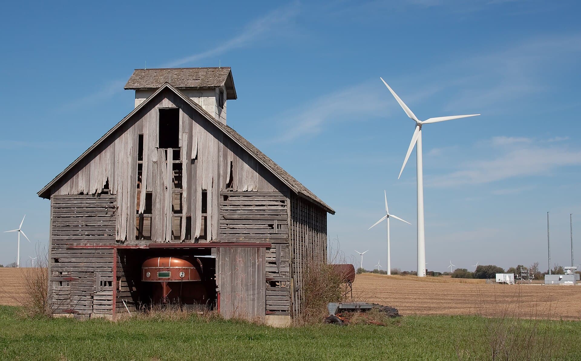 Un hambar vechi și mai multe turbine eoliene pe uscat, într-un peisaj rural. (Foto de arhivă: Dori / CC BY 2.5, Wikimedia Commons)