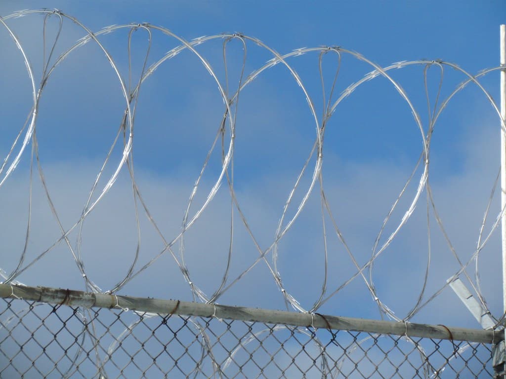 Gard de sârmă ghimpată, probabil în jurul unei unități de detenție, pe fundalul cerului. (Foto de arhivă: katerha / BY 2.0, Openverse)