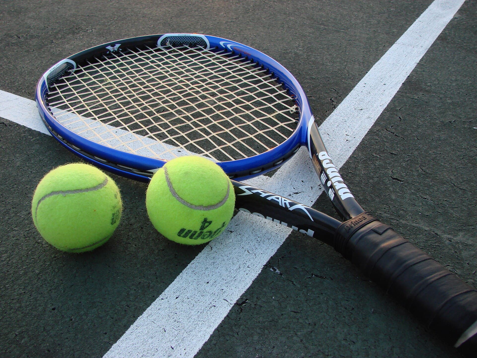 Două rachete de tenis și două mingi de tenis pe un teren de tenis. (Foto de arhivă: Vladsinger at English Wikipedia / CC BY-SA 3.0, Wikimedia Commons)
