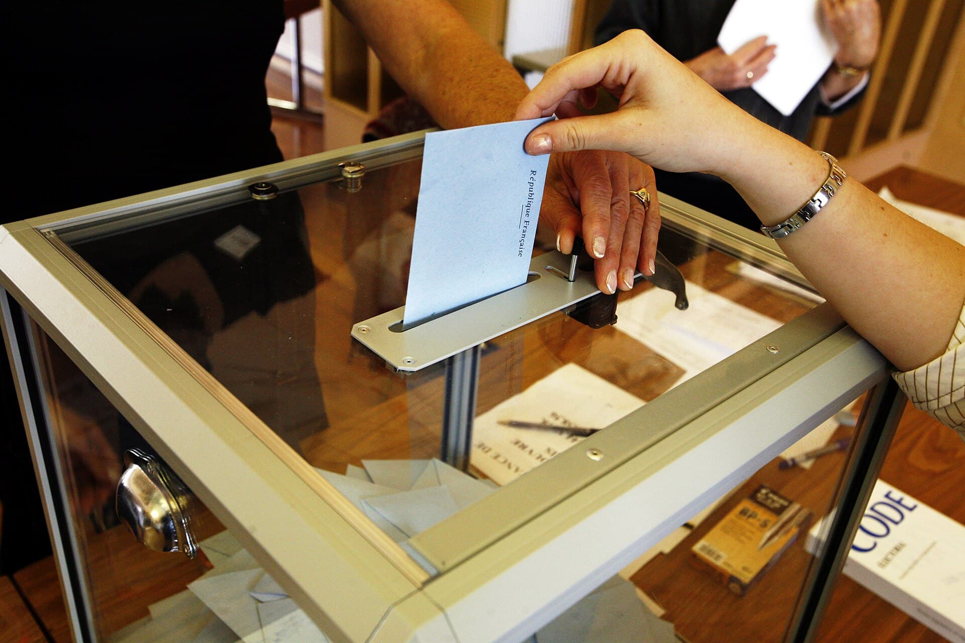 O persoană introduce un buletin de vot într-o urnă transparentă, în timpul unui scrutin. (Foto de arhivă: Rama / CC BY-SA 2.0 fr, Wikimedia Commons)