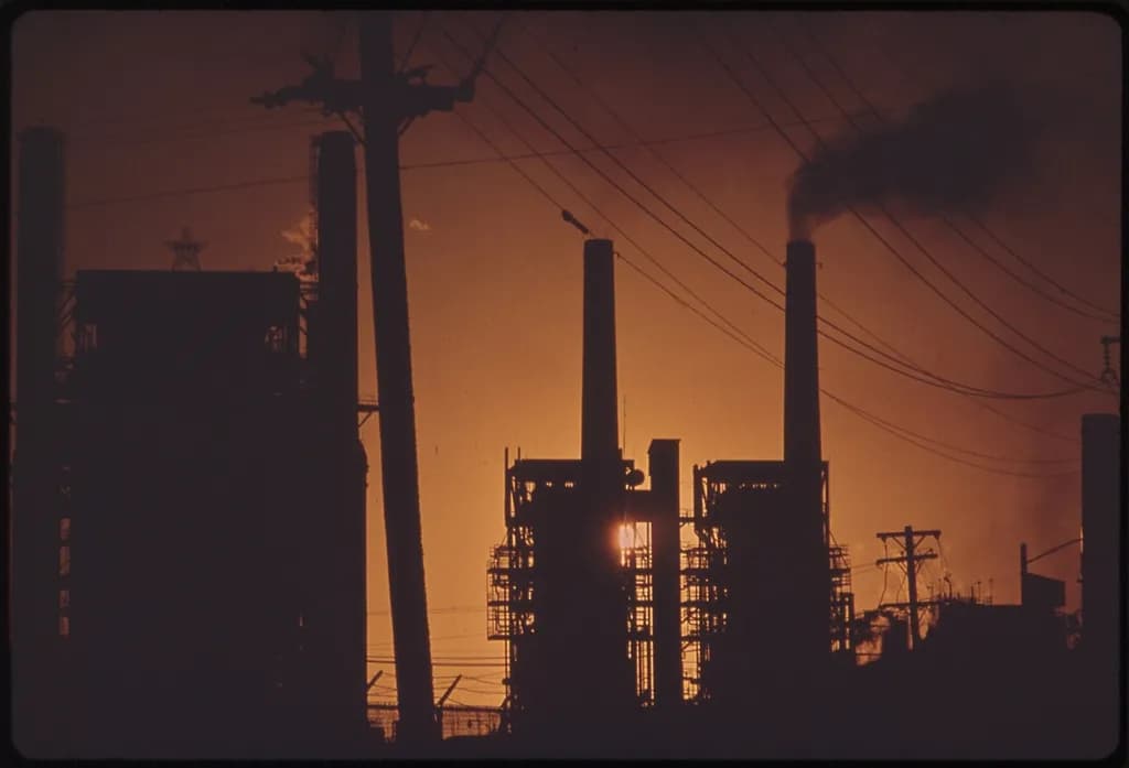 Se vede o instalație industrială de rafinare, cu coșuri de fum și fum dens, fotografiată la apus. (Foto ilustrativă: U.S. National Archives / CC0 1.0, Openverse)
