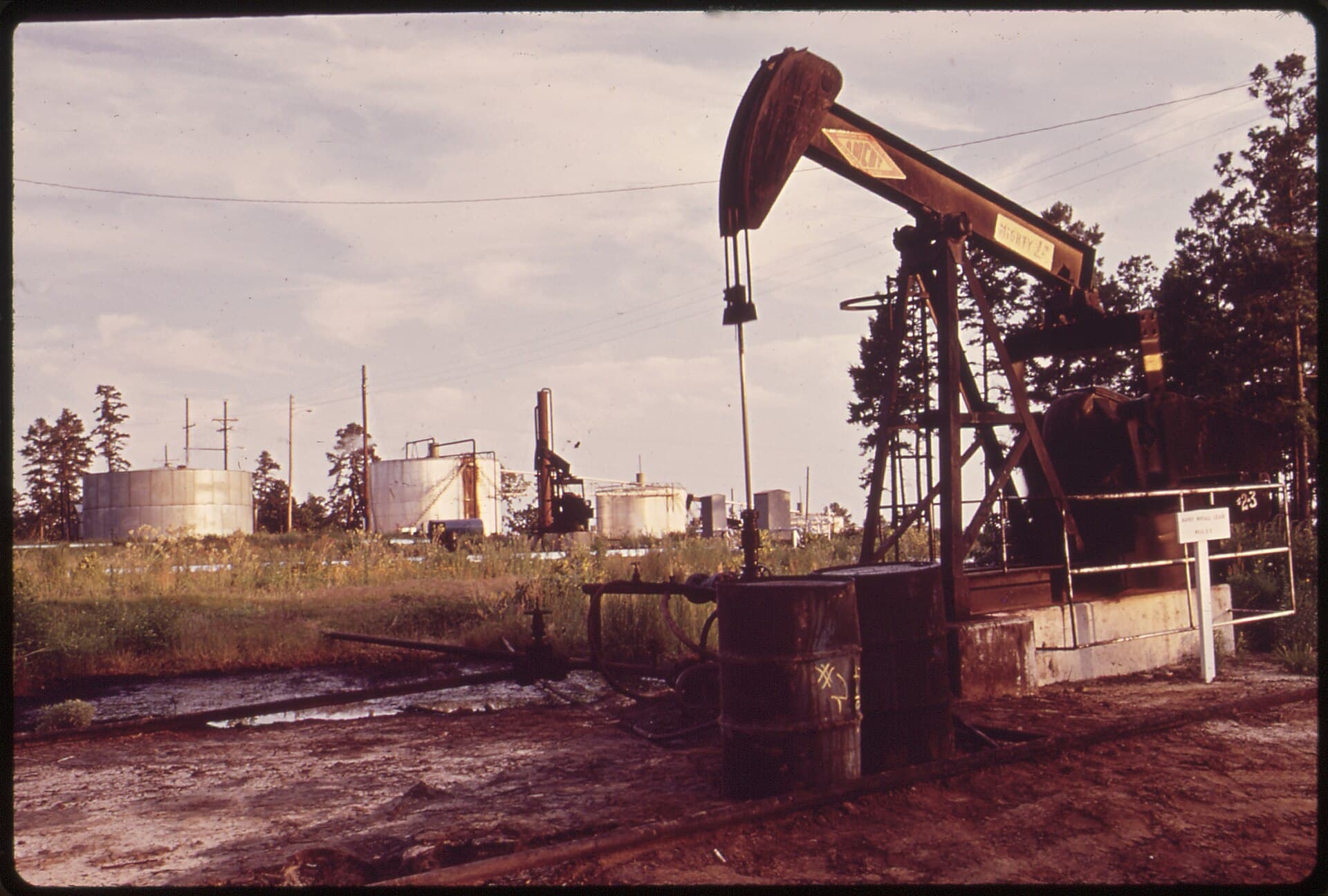 O sondă petrolieră cu pompă de extracție și rezervoare industriale, într-o zonă petrolieră. (Foto de arhivă: Marc St. Gil / Public domain, Wikimedia Commons)