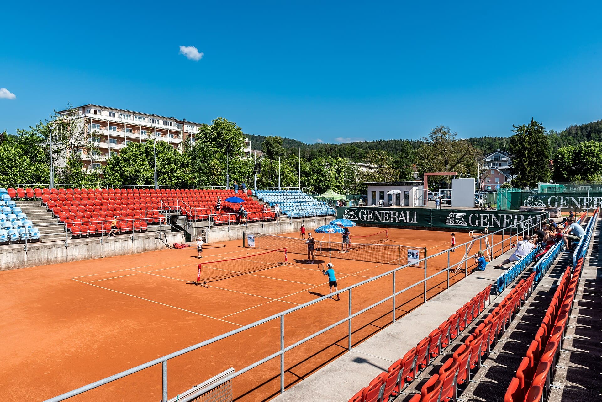 Un teren de tenis pe zgură, cu tribune și jucători în timpul unui meci. (Foto de arhivă: Johann Jaritz / CC BY-SA 4.0, Wikimedia Commons)